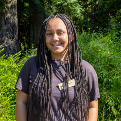 EYA staff Nikayla Allen smiling in front of greenery.