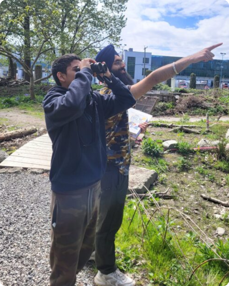 Two youth participants doing a birding exercise by observing with a pair of binoculars and pointing into the distance.