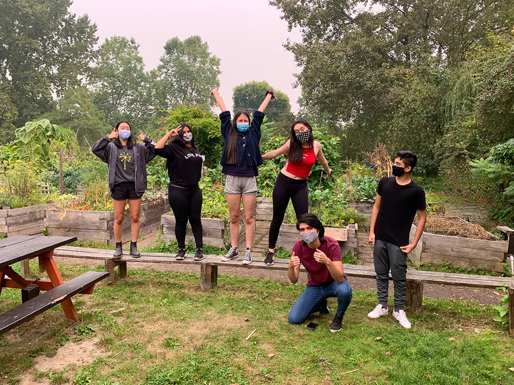 A group of youth are standing and posing outside surrounded by gardening boxes.