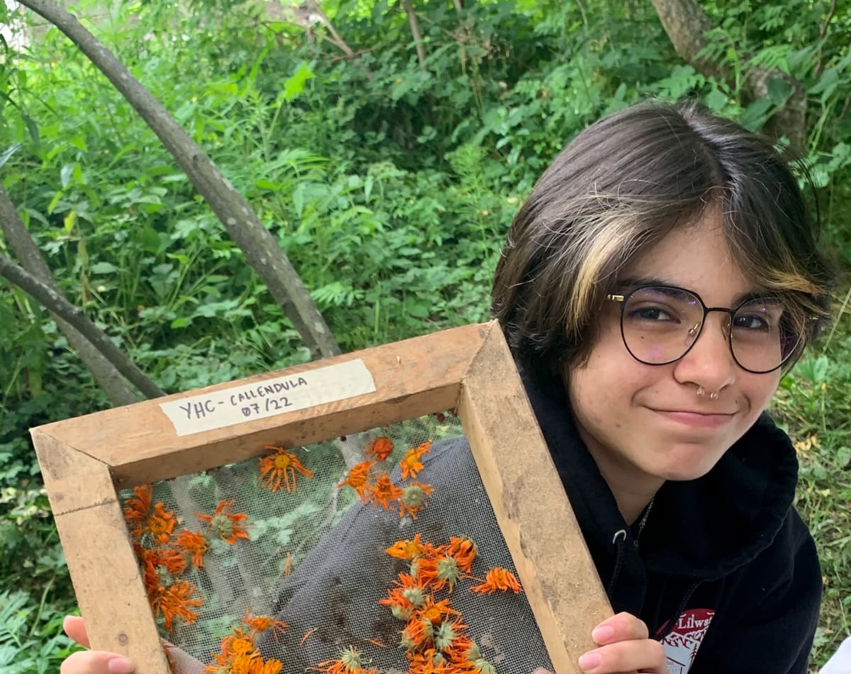 A close up shot of a youth participant who is outside and holding a frame with calendula flowers.