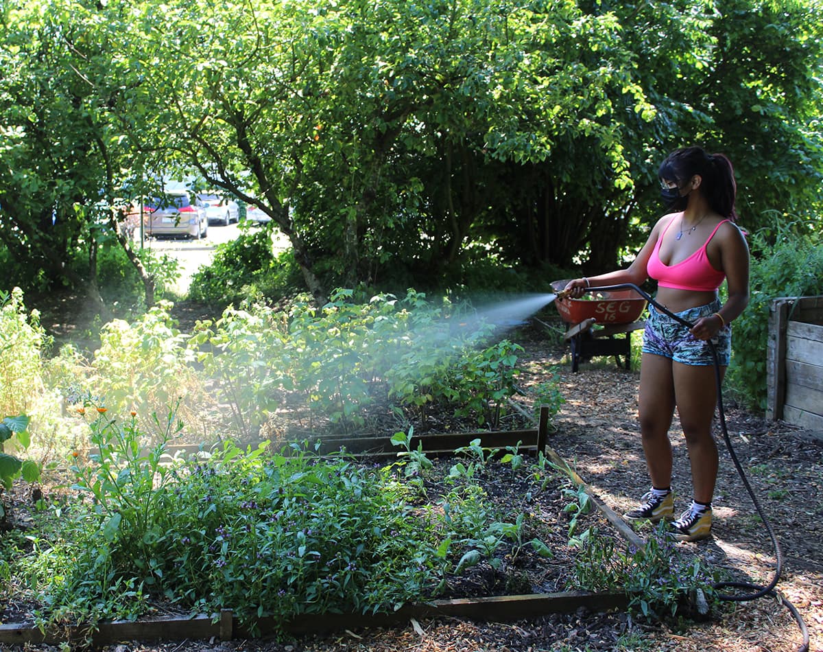 A young woman is standing outside watering a garden.